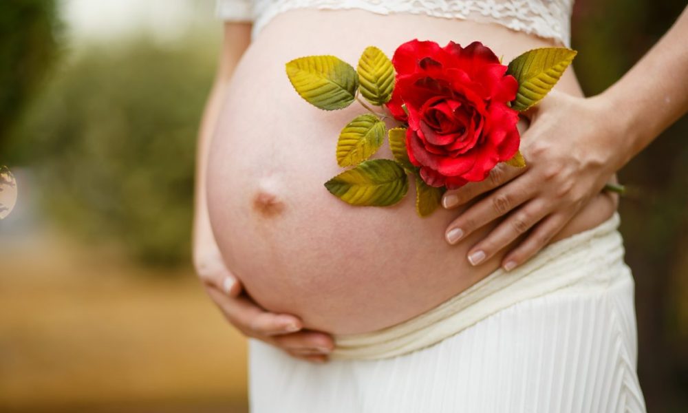 pregnant woman showing belly holding flower